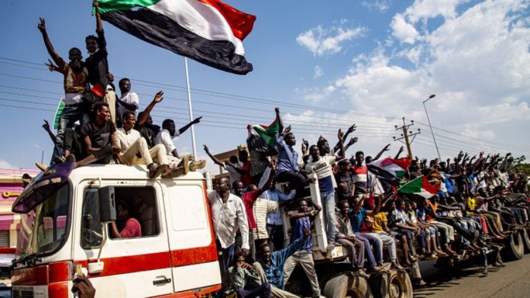 An image of men riding on a truck and waving the Sudanese flag