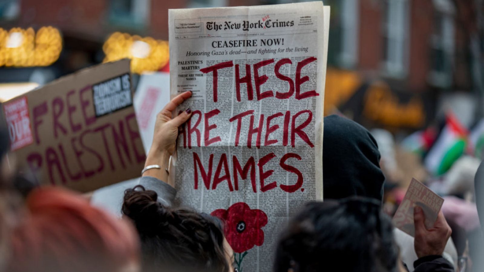image of protester holding up a newspaper with the words &quot;These are their names&quot; written on it