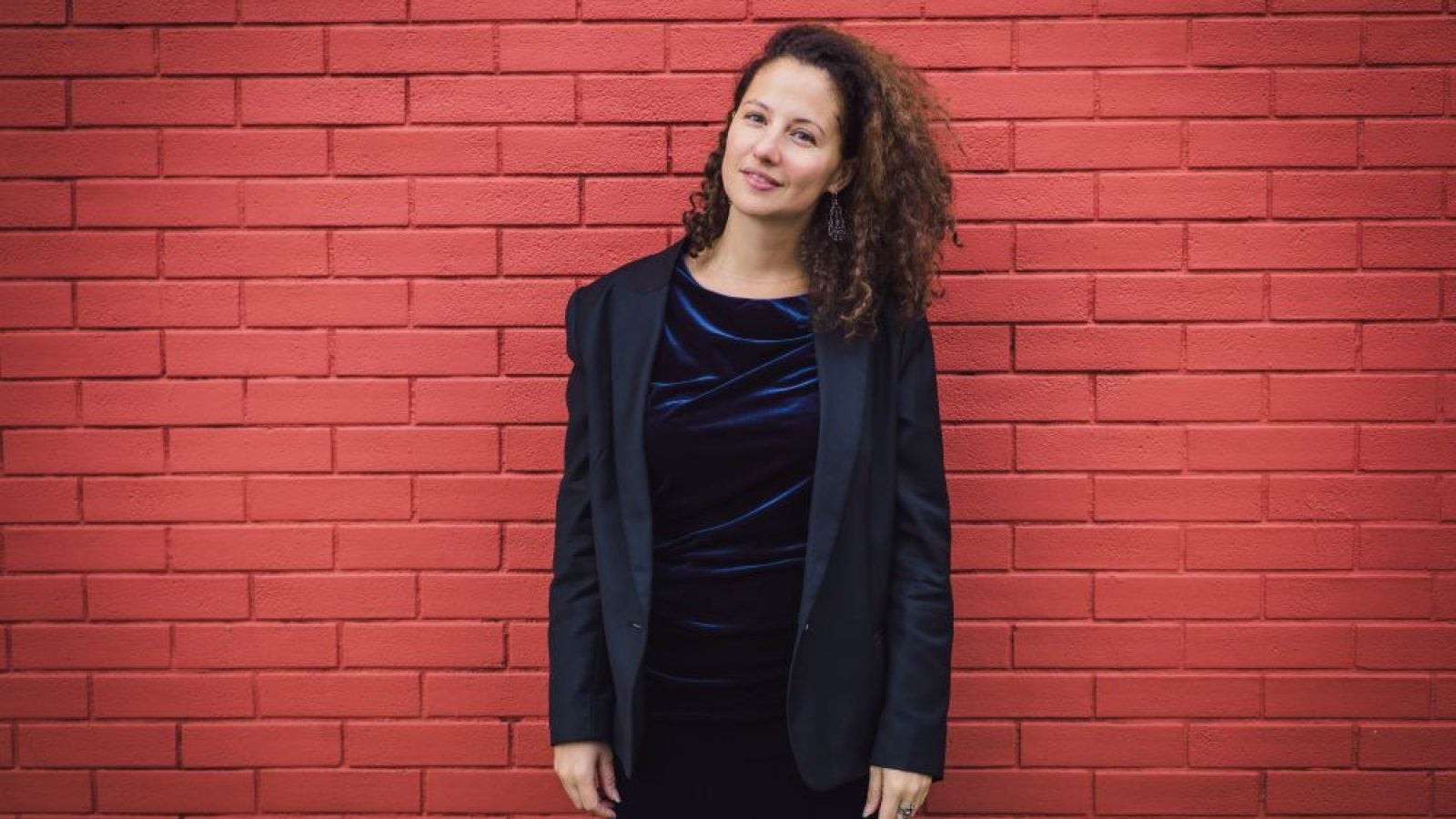 Dorothee Kellou standing in black suit in front of brick wall