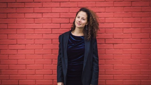 Dorothee Kellou standing in black suit in front of brick wall