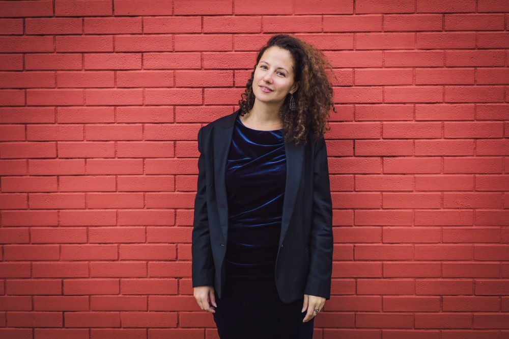 Dorothee Kellou standing in black suit in front of brick wall